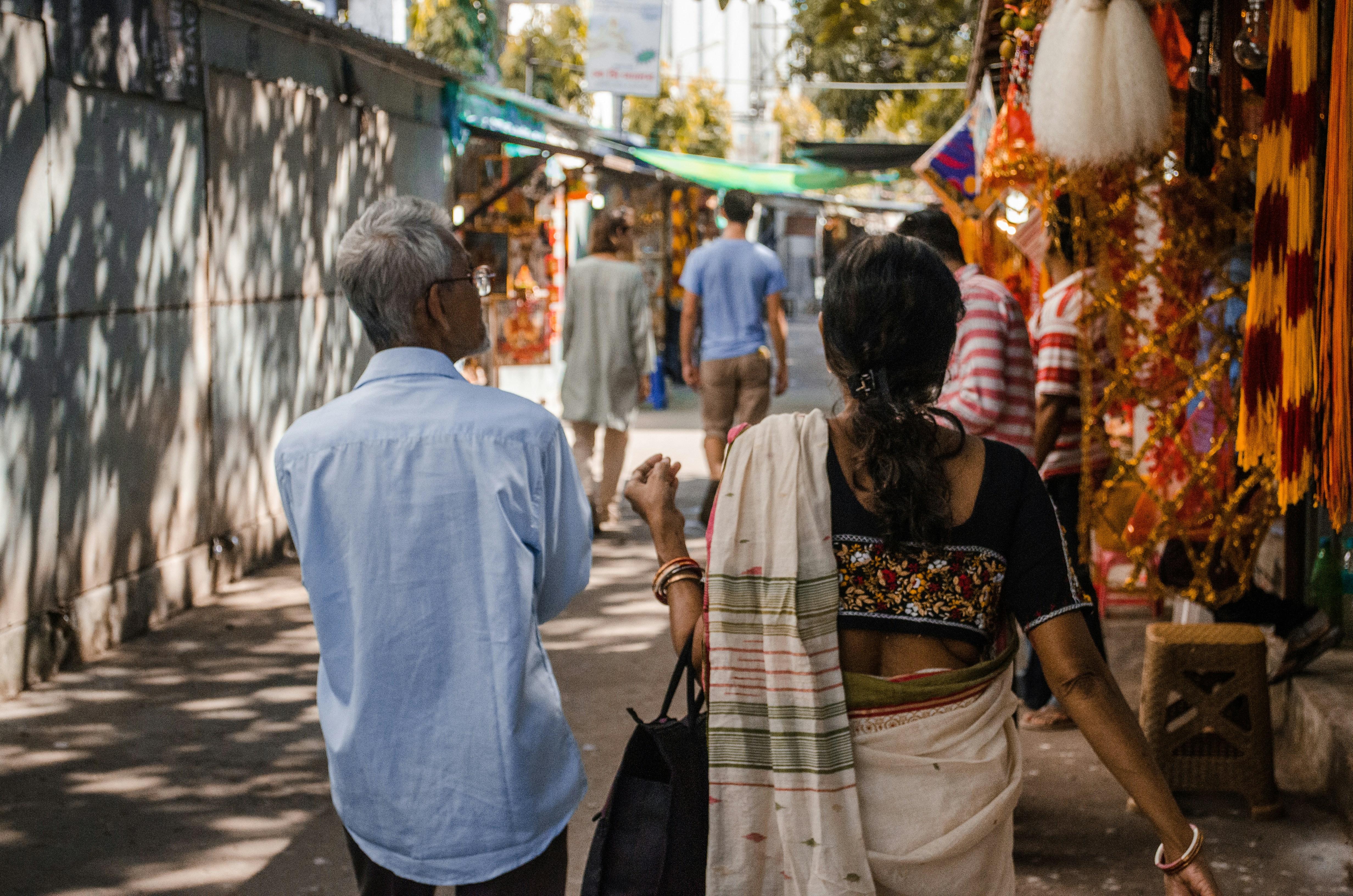 A man with silver hair wearing a blue shirt walking beside a woman wearing a saree and carrying a bag in her left hand. Photo by Carolina Avinceta on Unsplash