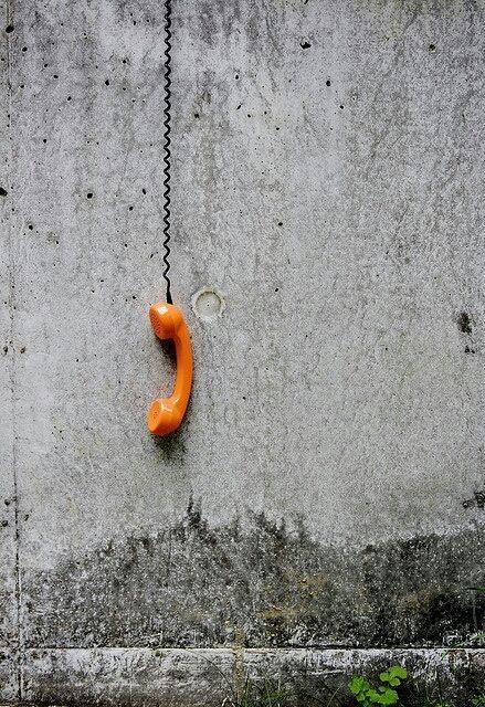 Orange analogue phone hanging by its wire on a concrete wall