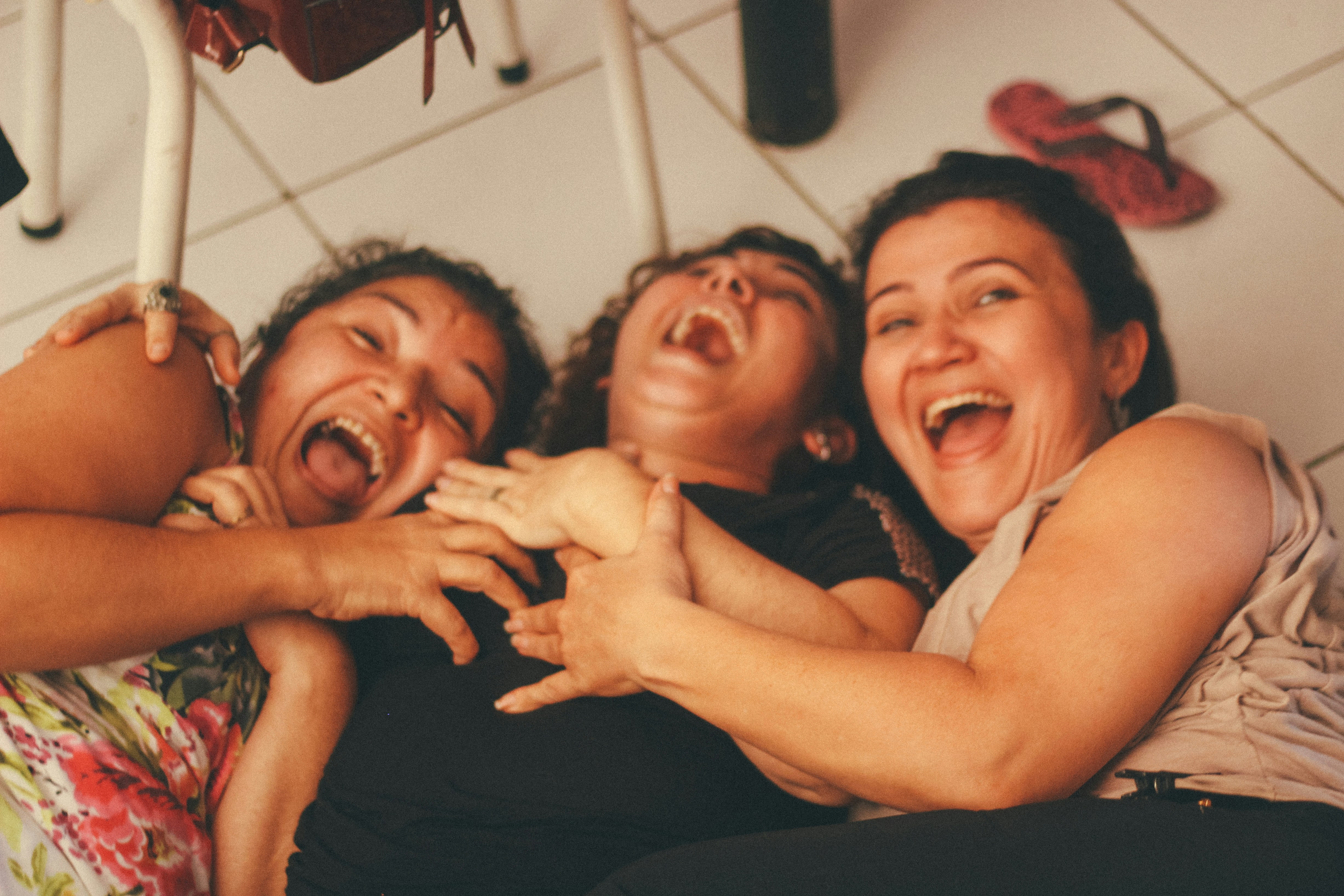 Three women rolling on the floor and laughing. Image by Igor Rodrigues on Unsplash
